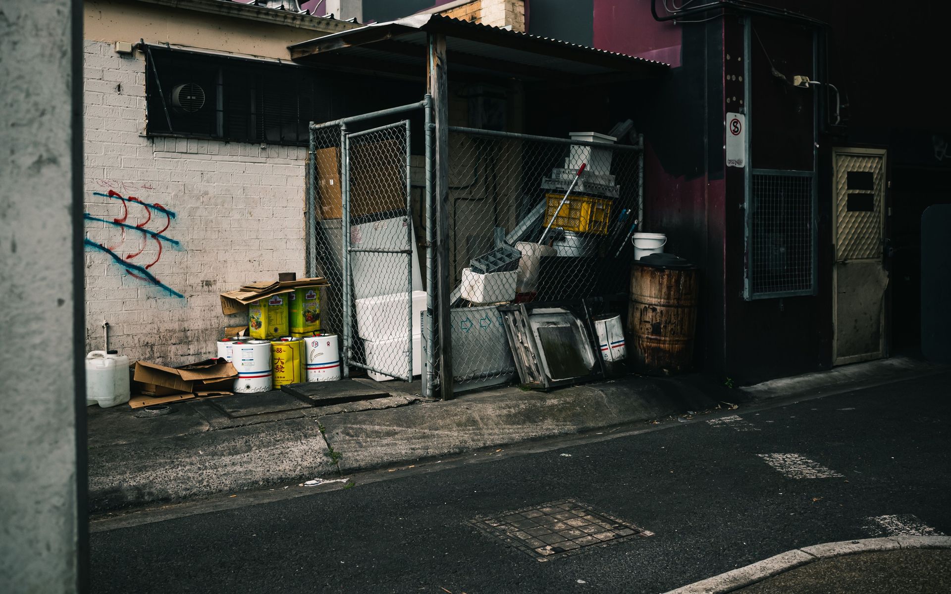 A gritty urban alleyway featuring industrial waste, graffiti, and dim lighting.