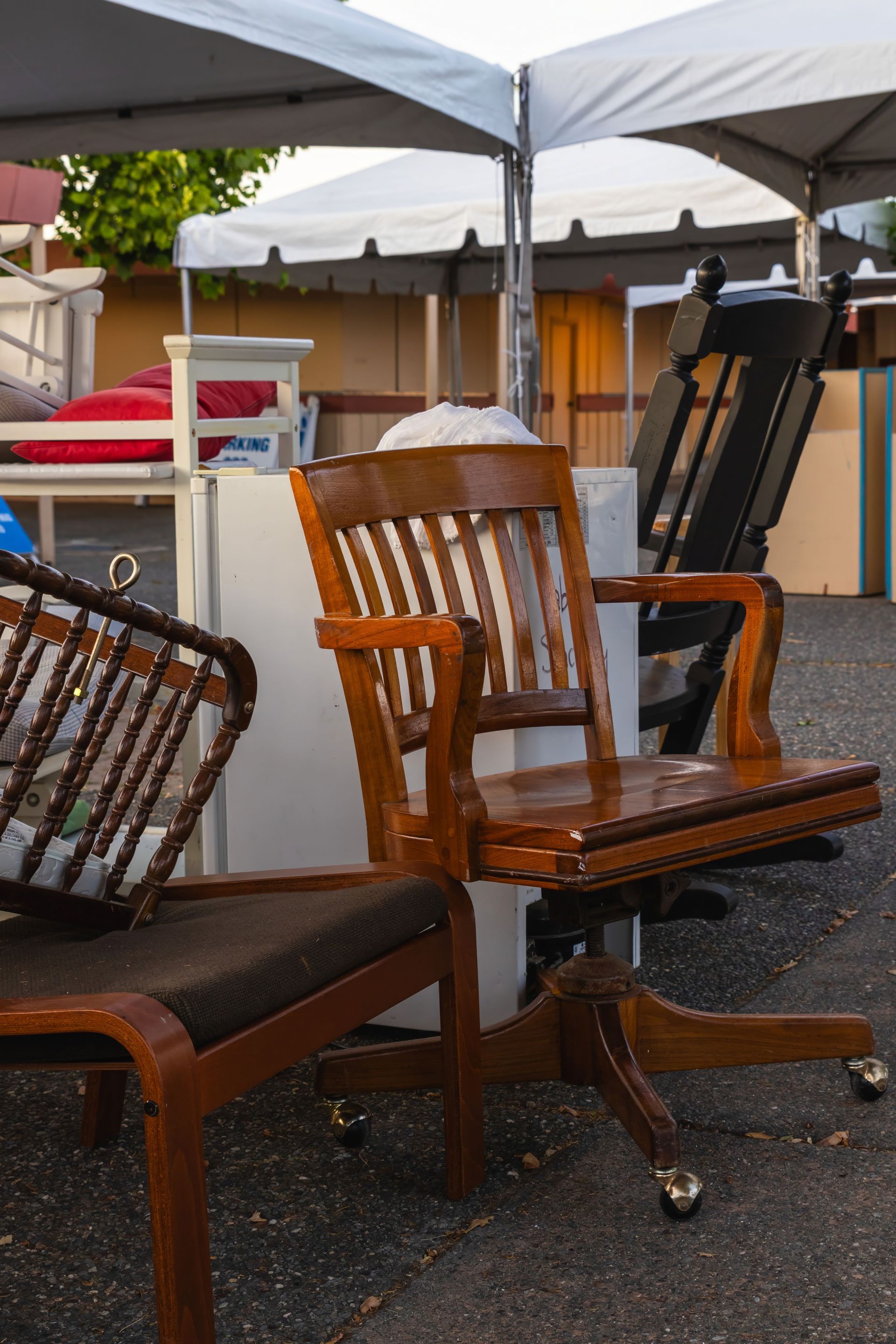 Collection of vintage wooden chairs on display at an outdoor market under a tent.
