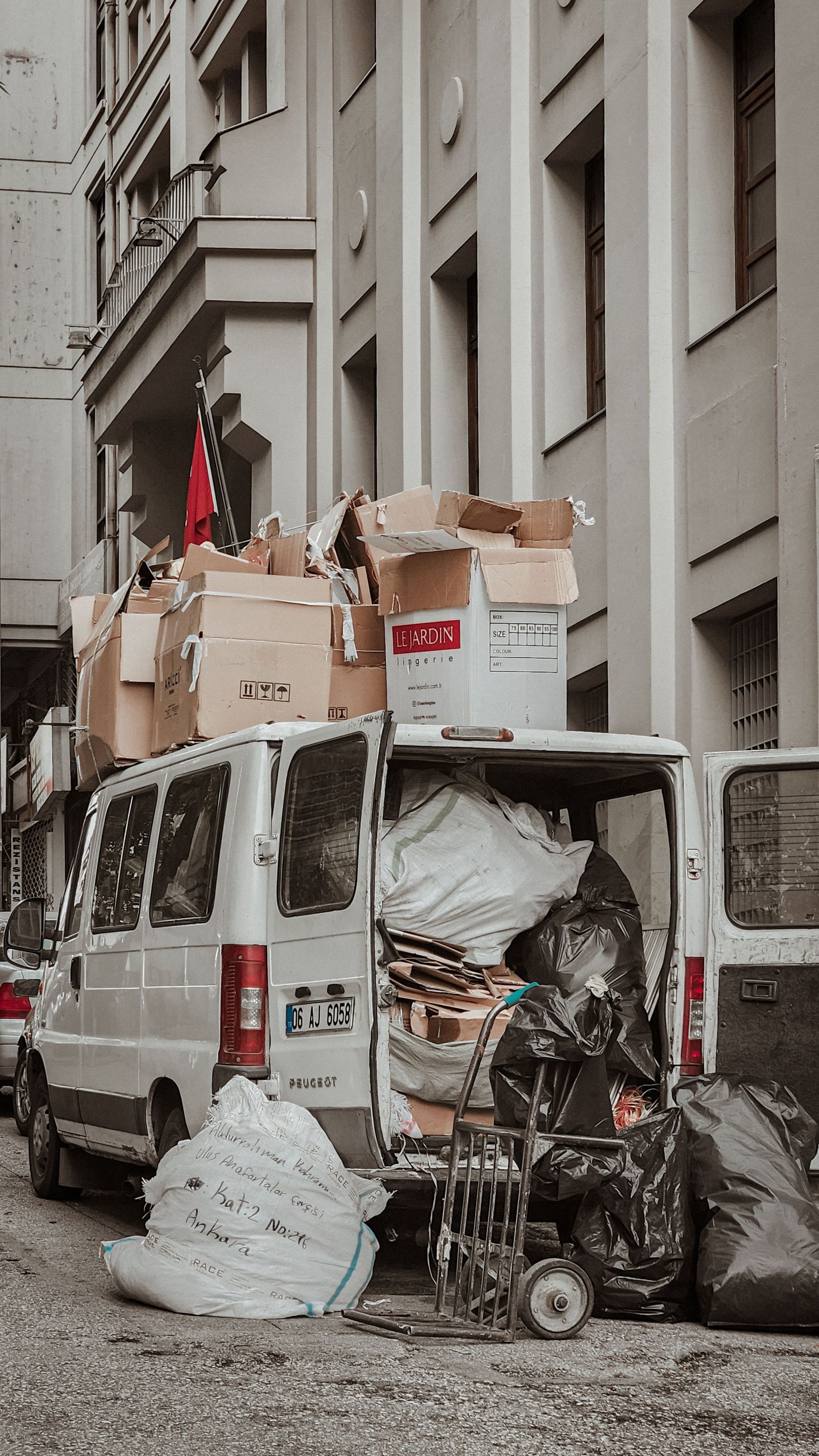 A white van loaded with cardboard boxes and bags in a crowded alleyway, illustrating urban storage challenges.